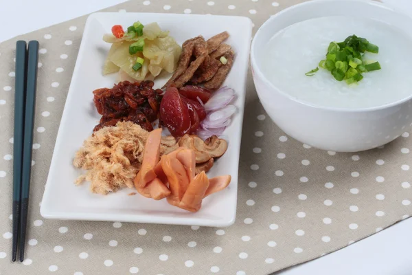 Pirinç gruel ve garnitür kahverengi napery üzerinde. (Kurutulmuş rendelenmiş domuz eti, Çin sosis, gevrek balık, sosis, kızarmış bebek istiridye, dilimlenmiş kırmızı soğan, turşu Çin lahanası, Baharatlı sardalya salatası ve arpacık )