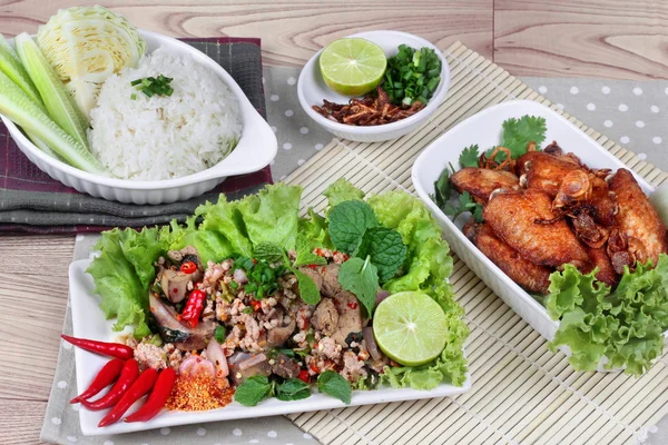 Nasi lengket disajikan dengan ayam goreng dan salad herbal pedas campuran ayam dan hati pada bambu dan kayu. Tampilan samping . — Stok Foto