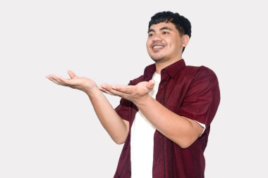 Avuç içleri açık, neşeli genç bir adam, kırmızı bir günlük gömlek giyiyor, açık gri bir arka planda izole edilmiş,.