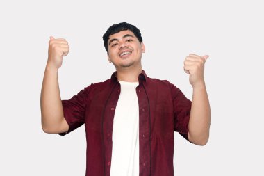 Neşeli genç adam onaylıyor iki eliyle başparmağını kaldırıyor, günlük kırmızı bir gömlek giyiyor, temiz beyaz bir arka planda izole edilmiş, Olumlu Geri bildirim ve Başarı kavramı.