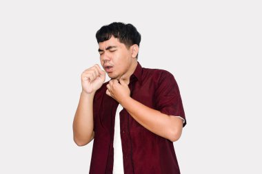 Young man in red shirt coughing with hand to mouth and chest, expressing discomfort on a white background, Illness Concept.