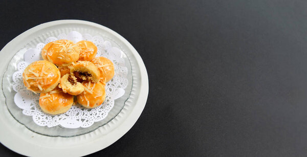 Delicious golden brown pineapple tarts, traditional Indonesian cookies with sweet jam filling, served on a white plate against a dark background, Festive Dessert Concept.
