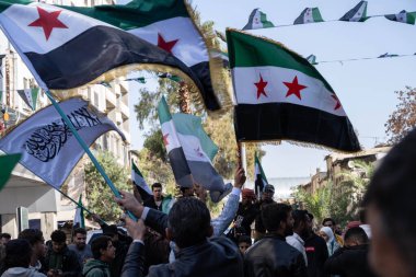 Şam, Suriye. 7 Aralık 2025. Bir grup erkek ve insan, halka açık bir gösteri ya da kutlama sırasında Suriye bayraklarını sallayarak bir şehir caddesinde toplandı..