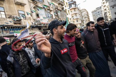 Şam, Suriye. 7 Aralık 2025. Siyah kapüşonlu bir adam, Şam caddesinde kalabalıkla yürürken kırmızı bir ip ya da ilmik tutuyor..