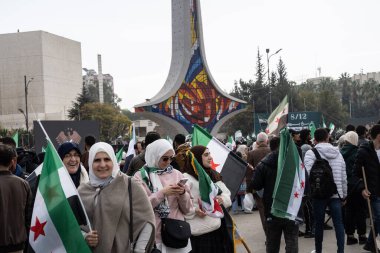 Şam, Suriye. 8 Aralık 2025. Gülen kadınlar, bir şehir meydanında bir mozaik heykeli olan büyük bir halk toplantısında Suriye bayrakları taşıyor.