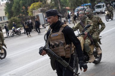 Şam, Suriye. 8 Aralık 2025. Silahlı adamlar taktik teçhizat devriyesinde gündüz vakti şehir caddesinde motosiklet sürüyorlar..