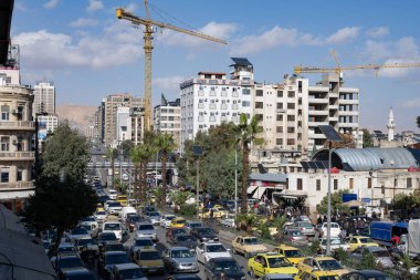 Şam, Suriye. 7 Aralık 2025. Yoğun trafiği olan işlek bir şehir kavşağı. Tarihi bir taş kale yakınında çok sayıda araba ve yaya var..