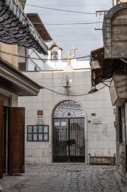 Şam, Suriye. 10 Aralık 2025. Aziz Paul Kilisesi Kilisesi Hristiyan haçlarıyla kaplı bir kilisenin beyaz taş kapılı girişine giden taşlarla döşenmiş Şam geçidine bakıyor.