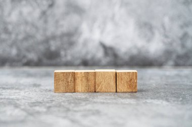 A row of four blank wooden blocks sits on a textured gray surface, perfect for displaying letters, numbers, or symbols in creative projects.