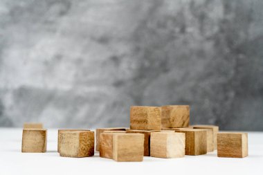 A collection of wooden blocks are arranged on a white surface, set against a textured gray background, creating a minimalist and geometric composition.