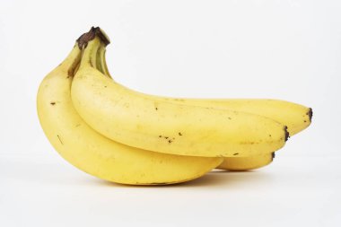 Üç olgun sarı muz, temiz beyaz bir arka planda izole edilmiş doğal bir kümede otururlar..