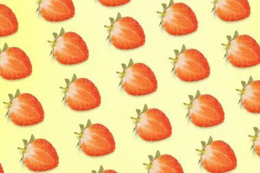 Parlak kesim çilek yarıları tek renkli sarı arka plana karşı canlı ve tekrarlayan bir desen oluşturur..