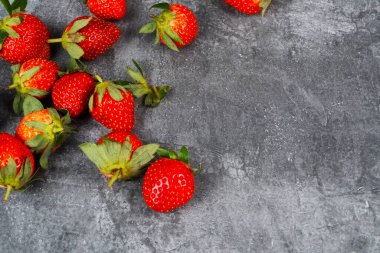Kırmızı çilek yığını koyu dokulu arka planın sol alt köşesinde duruyor. Mesaj için boşluk bırakıyor..