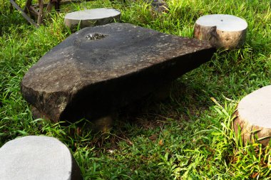 Kırsal taş masa, yuvarlak koltuklarla çevrili çimenlerin arasında oturur.