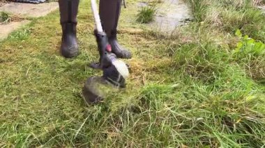 Close-up footage of a person cutting overgrown grass with an electric trimmer outdoors. showing movement, grass debris and the trimming process.