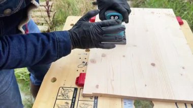 A man processes a wooden board with a cordless sander. Construction tools, woodworking, grinding, machining, construction.