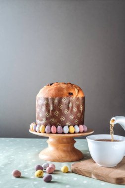 Easter bread, panettone with chocolate eggs on the wooden stand and a cup of tea. Easter concept