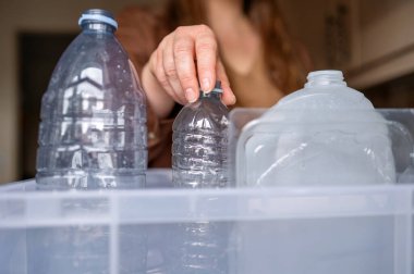 Mutfakta plastik şişeyi eve geri dönüşüm kutusuna koyan bir kadının yakın plan çekimi, sorumlu bertaraf etme kavramı ve sürdürülebilir günlük rutin.
