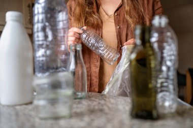 Kadın boş bir plastik şişeyi geri dönüşüm çantasına koyup atık ayıklama sürecini ve ev içinde çevre dostu alışkanlıkları gösteriyor..
