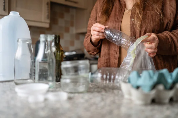 Kadın boş bir plastik şişeyi geri dönüşüm çantasına koyup atık ayıklama sürecini ve ev içinde çevre dostu alışkanlıkları gösteriyor..