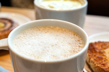 Kahve dükkanının ahşap masasında sütlü köpüklü kremalı kapuçino. Sıcak sıcak atmosfer.