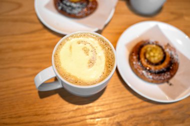 Şam fıstıklı sütlü latte, rahat bir kafede, ahşap masada tarçınlı rulo ile servis edilir. Tatlı ve özel kahve konsepti..