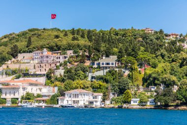 Türkiye 'nin İstanbul kentindeki İstanbul Boğazı' nda yaz mevsiminde, Türk ulusal bayrağı ve yeşil ormanıyla birlikte çok güzel binalar ve malikaneler inşa edildi. Bir Gemi Gezisinden Görünüm.