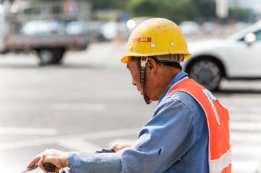 Çin 'in Shenzhen caddesinde güvenlik kaskı takan bir inşaat işçisi scooter kullanıyor..