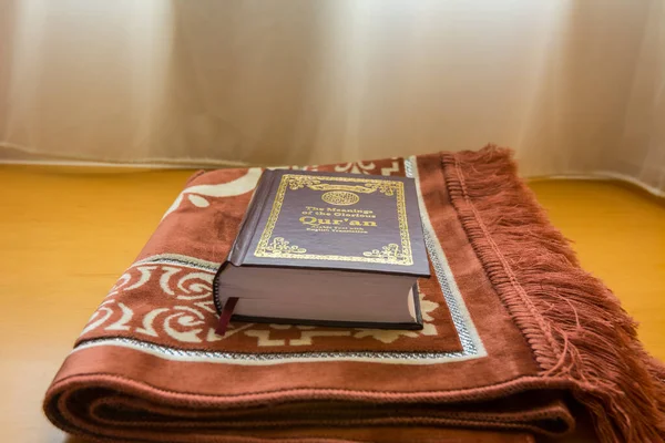 A holly Quran book on a traditional Arabic carpet at the window under sunlight at the room of hotel