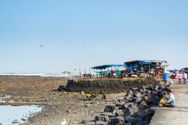 1431 yılında inşa edilen Hacı Ali Camii 'nin yanındaki kirli kıyı şeridinde bir restoran ve gecekondu mahallesi Hindistan' ın en ünlü camilerinden biridir.