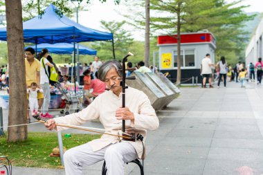 Orta yaşlı Çinli sokak müzisyeni Çin 'in Shenzhen kentindeki Central Park' ta geleneksel müzik enstrümanı Erhu (Çin keman) çalıyor.