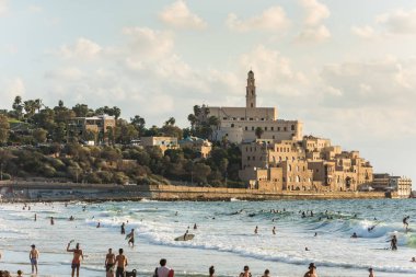 Birçok turist ve yerli mavi Akdeniz 'de yüzüyor ve tatillerini İsrail' in Tel Aviv kentindeki eski Jaffa şehrinin arka planında geçiriyorlar. 