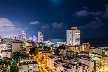 İsrail 'in Tel Aviv limanı yakınlarındaki kumsalda modern gökdelenler ve lüks otellerle Tel Aviv şehrinin gece hava manzarası.