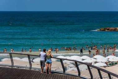 Turistleri ve yerlileri izleyen iki turist, güneşli bir günde Akdeniz 'de yüzüyor ve tatillerini İsrail' in Tel Aviv plajında geçiriyorlar..