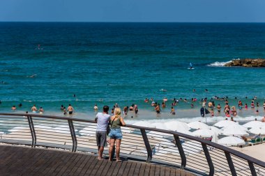Turistleri ve yerlileri izleyen iki turist, güneşli bir günde Akdeniz 'de yüzüyor ve tatillerini İsrail' in Tel Aviv plajında geçiriyorlar..