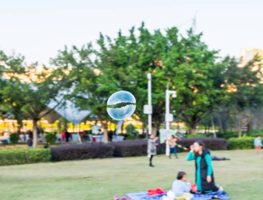 Bir sabun köpüğü, sonbaharda bir yerleşim alanının yakınında ağaç ve çayır ile parkta uçuyor. 