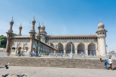 Muslim pilgrims walking into the Mecca Masjid mosque against blue sky and doves flying in sky, a famous monument in Hyderabad  clipart