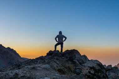 Kayalık dağın tepesinde duran erkek bir turist Tochal dağının renkli gökyüzüne karşı sonbaharda Darband vadisinde güneşin doğuşunu seyrediyor.. 