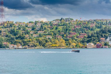 İstanbul Boğazı boyunca uzanan ormandaki modern binalar güneşli bir günde feribottan arka planda bulutlu bir gökyüzü ile Türkiye 'de