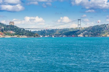 Çağdaş yapılar ve Rumeli Kalesi ve İstanbul Boğazı 'ndaki Fatih Sultan Mehmet Köprüsü güneşli bir günde arka planda bulutlu gökyüzü ile feribottan Türkiye' ye iniyor.