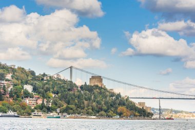 Çağdaş yapılar ve Rumeli Kalesi ve İstanbul Boğazı 'ndaki Fatih Sultan Mehmet Köprüsü güneşli bir günde arka planda bulutlu gökyüzü ile feribottan Türkiye' ye iniyor.