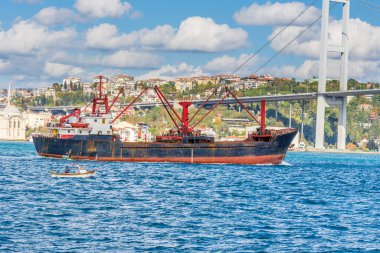 Güneşli bir günde İstanbul, Türkiye 'de arka plan bulutlu mavi gökyüzü ve mavi deniz ile Boğaz Boğazı' nın arka planına sahip Boğaz Köprüsü 'nün altında gemi yelken açıyor. 