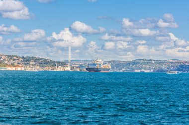 Güneşli bir günde İstanbul, Türkiye 'de arka plan bulutlu mavi gökyüzü ve mavi denizle birlikte Boğaz Boğazı' nın arka planında yer alan Boğaz Köprüsü 'nden geçen ticaret gemisi. Mavi Hindi konsepti.