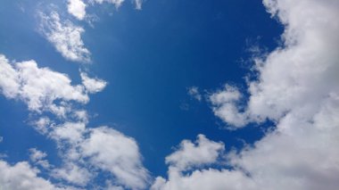 Yumuşak beyaz bulutlar derin mavi gökyüzünde süzülür, sakin ve görsel olarak çekici bir gündüz manzarası yaratır..