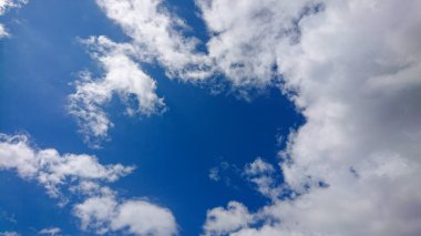 İnce ve kabarık bulutlar canlı mavi bir gökyüzünde sürükleniyor, barışçıl ve görsel olarak çarpıcı bir manzara yaratıyor..