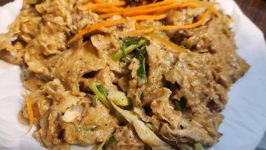 Kothu roti 'ye yakın plan, doğranmış düz ekmek, baharatlarla kızartılmış, beyaz bir tabakta servis ediliyor, yemek fotoğrafçılığının dokusunu ve lezzetini gösteriyor..