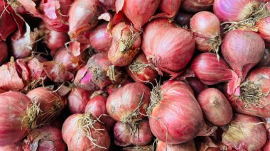 Bir yığın taze, çiğ, soyulmamış kırmızı soğanın tam kare makro görüntüsü doğal ve dokulu bir gıda pazarı arka planı yaratır..