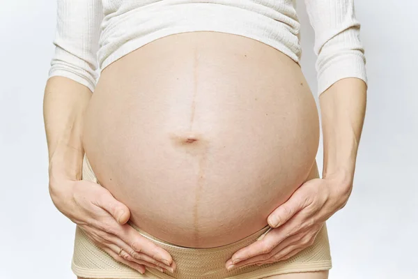 Una mujer embarazada sin rostro sostiene su vientre con sus manos. primer plano aislado. Cinturón de maternidad Embarazo Abdomen Apoyo Abdominal Binde. vista lateral y espacio de copia. — Foto de Stock