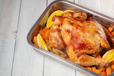 Beyaz ahşap arka planda havuç ve portakallı fırınlanmış tavuk. Yakın plan. 