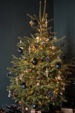 Siyah arka planda şık bir Noel ağacı. Ağaç siyah ve bej renkli yeni yıl oyuncaklarıyla süslenmiş. Ağacın altındaki kutularda hediyeler var..